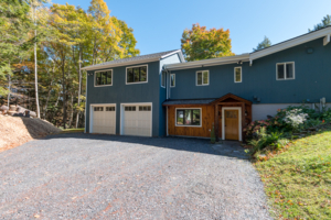 blue home with white garage doors and gravel driveway
