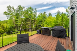 wooden deck with grill and black metal railing overlooking green scenery