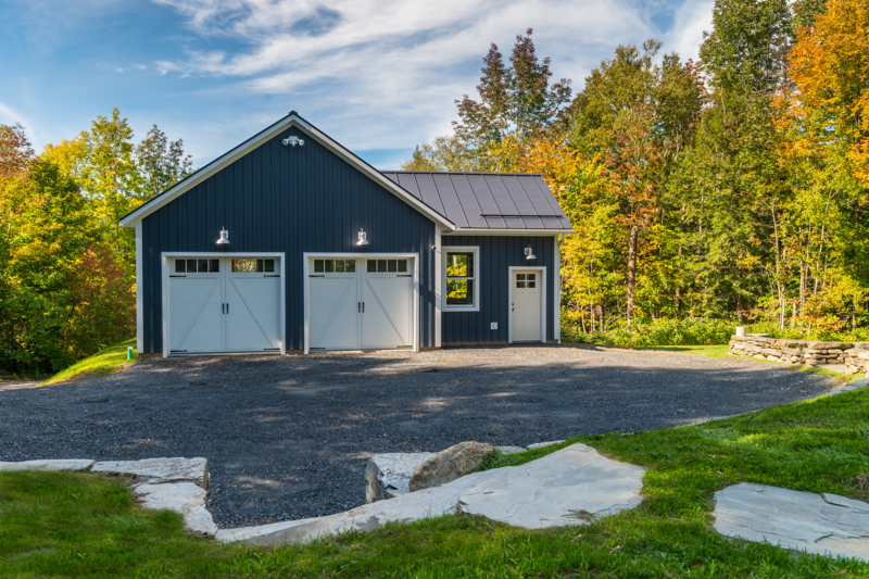 blue garage with wooden trim and gravel driveway